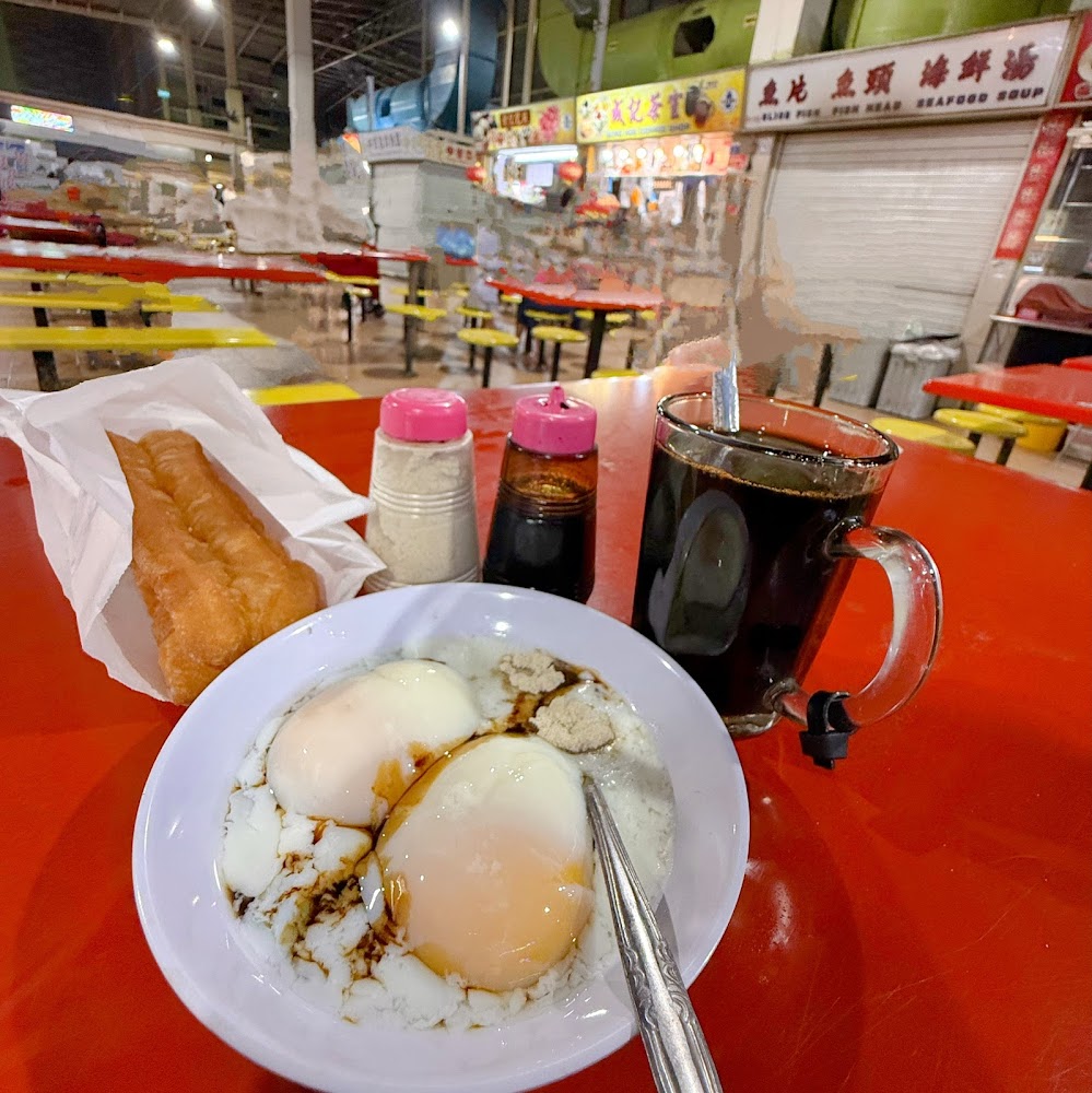 Breakfast set at Seng Kee with soft-boiled eggs, toast and kopi O on a red table, the hawker centre beyond